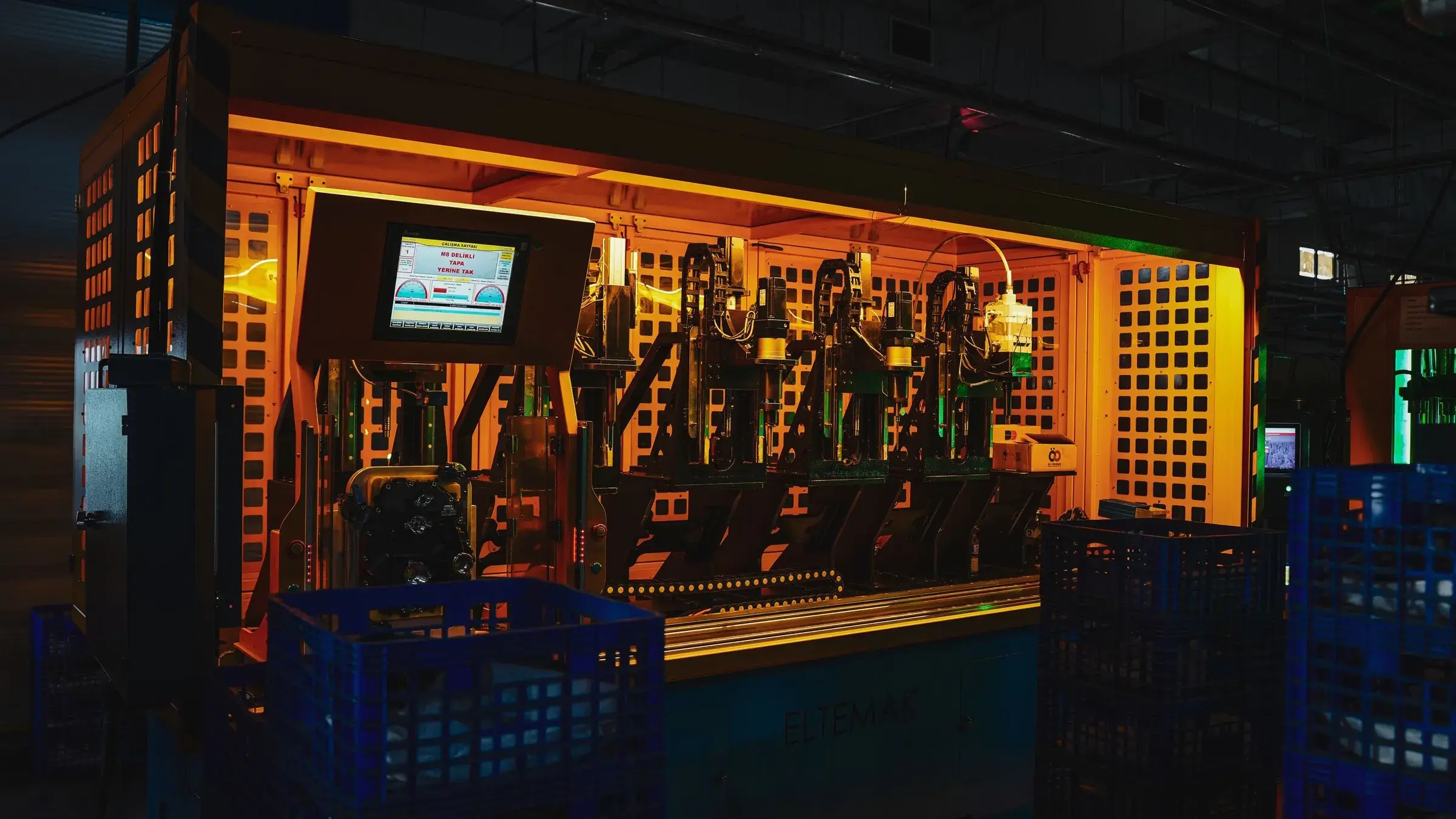 A machine shop floor at night, lit in amber by the light bars over a row of enclosed work cells.