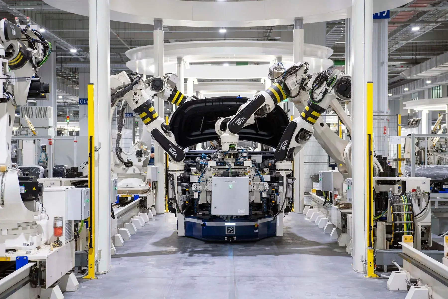A row of white robot arms working along an enclosed automotive assembly line.