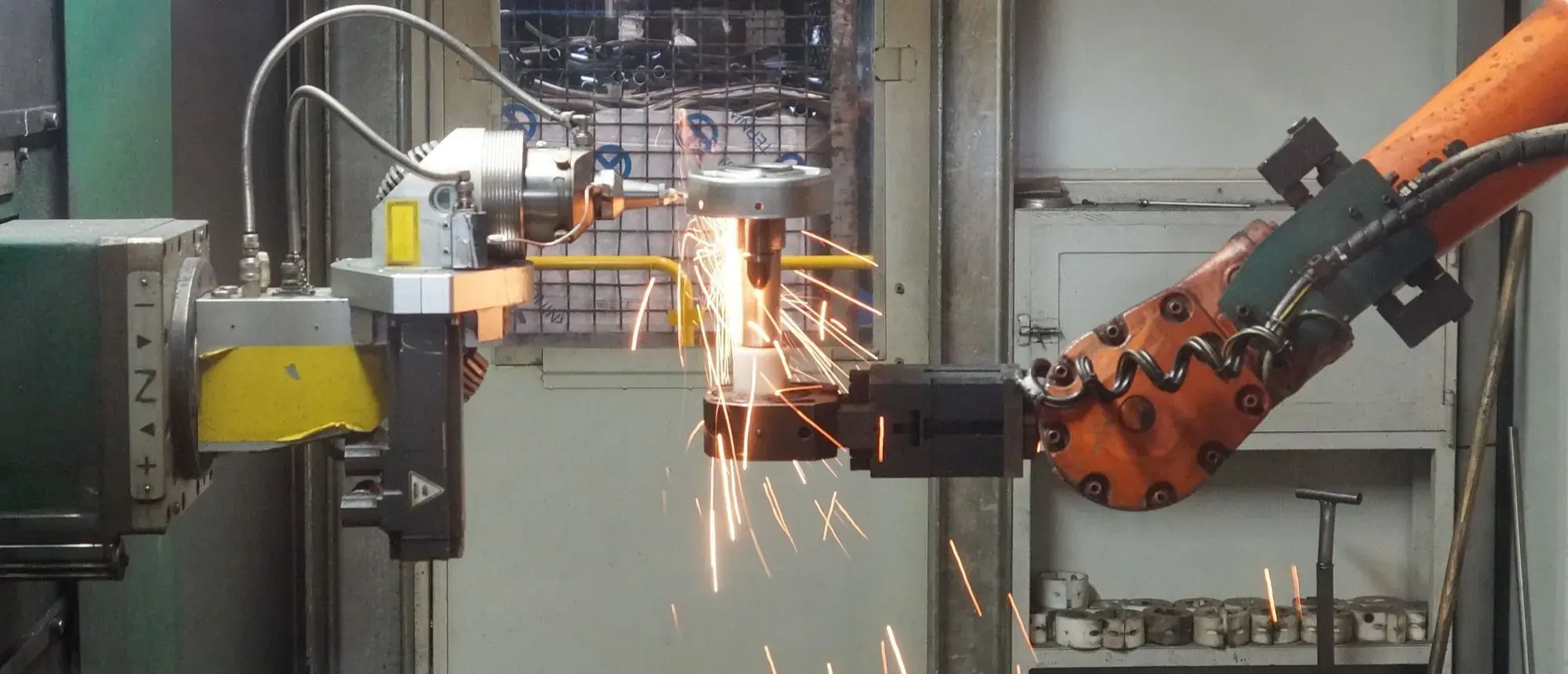 A robotic welding cell throwing sparks in a dark factory.