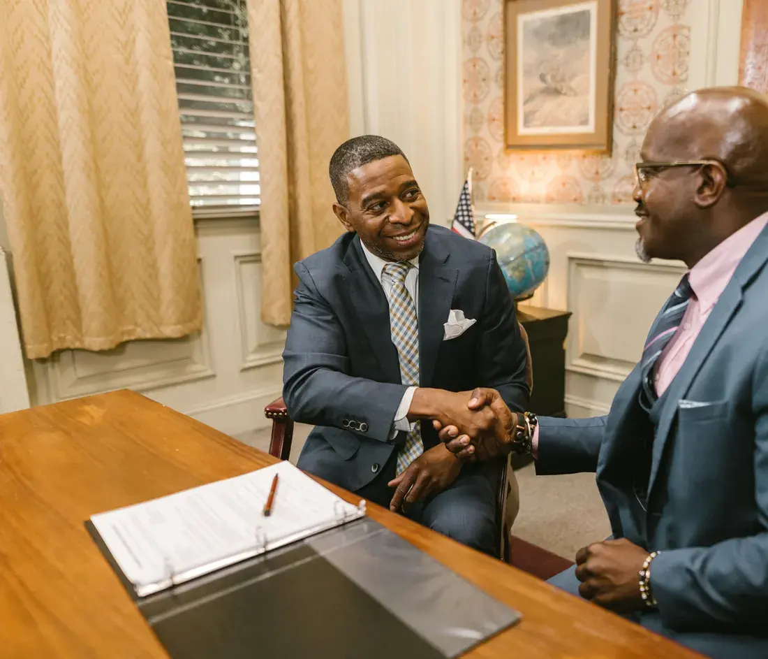 Two people shaking hands across a desk after a meeting.