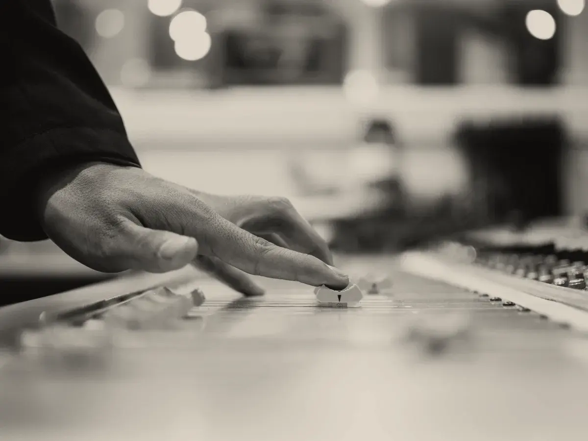 A hand working across a long desk of controls, the rest of the room out of focus.