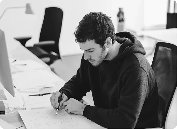 A member sketching a layout at a desk covered in paper
