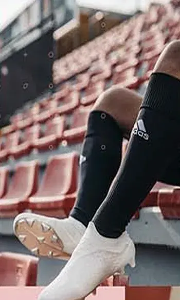 A white studded boot in profile on a stadium step, dark socks behind it