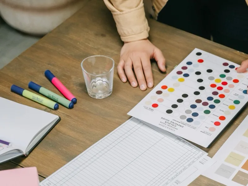 A hand marking up a printed colour chart with felt pens.
