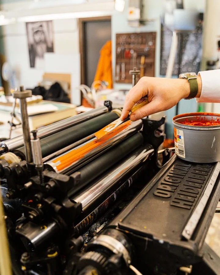 A hand rolling ink across a press roller in yellow and red.